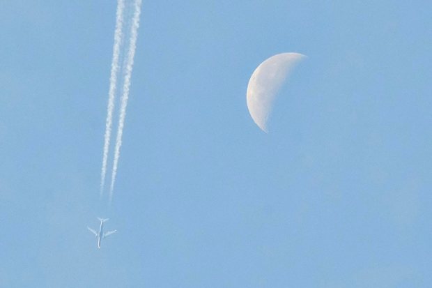 La lune et un avion dans le ciel bleu.
